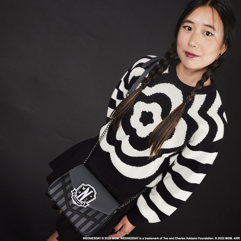 Woman wearing a black and white sweater with a black skirt looking up at the camera and wearing the Wednesday Addams Crossbody Bag